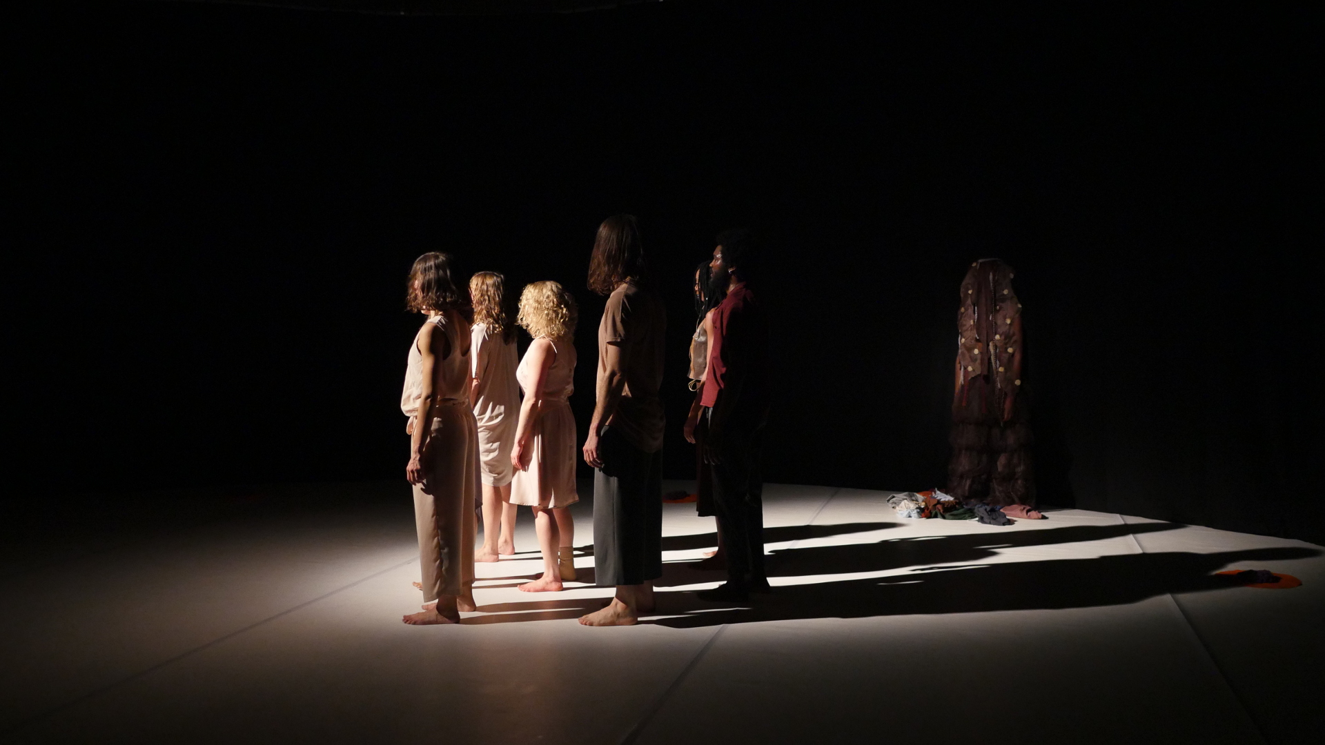 Dancers are standing on the stage, behind them is a dancer with a costume that resembles an entity of Afro-Diasporic religions.