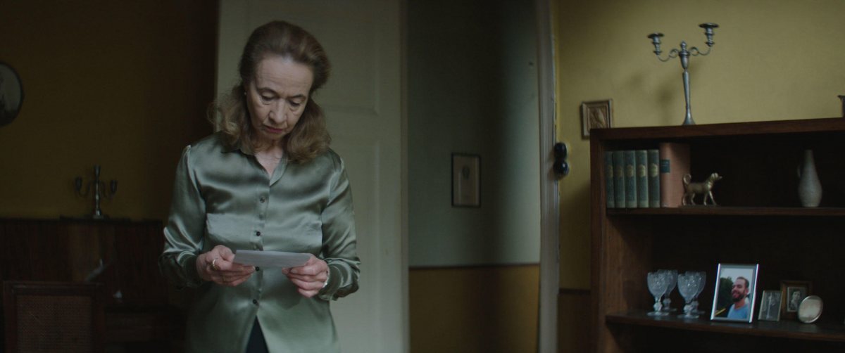 Woman reads a letter while standing in her living room.